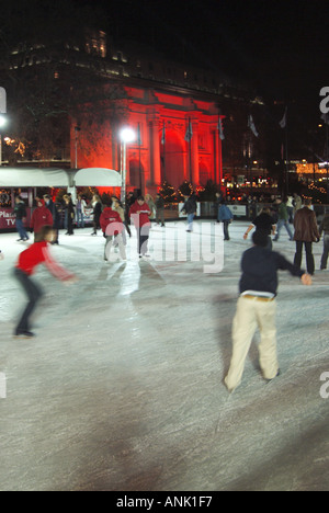 Skaters trying out the ice on Christmas winter season night ice skating rink with historic Marble Arch floodlit red beyond London West End England UK Stock Photo