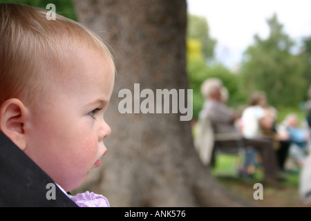 side view of pretty baby girl in Malvern park looking across picture with people in background Stock Photo