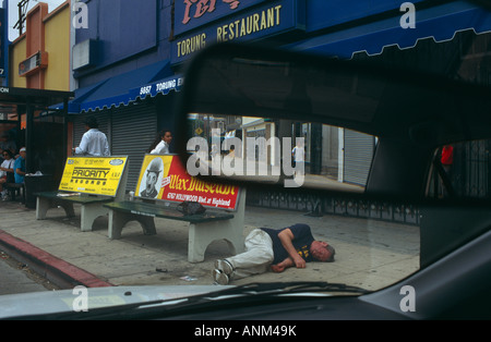 As normal life continues a man under the influence of alcohol lies unconscious in Hollywood near poster of tramp Charlie Chaplin Stock Photo