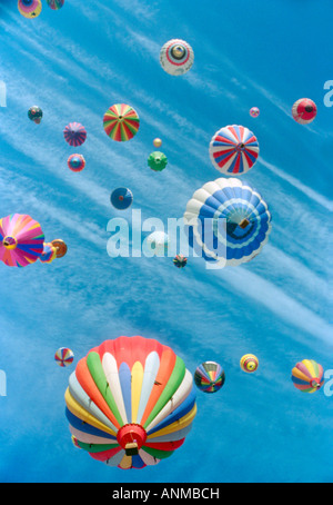 Numerous colorful hot air balloons with various patterns and shapes float amidst wispy white clouds across a bright blue sky. Stock Photo