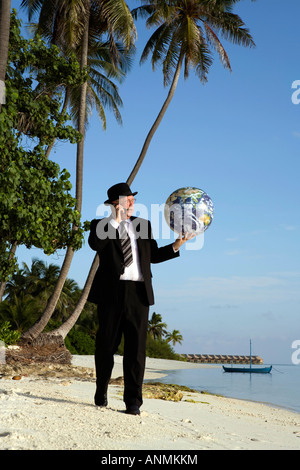 Maldives businessman on beach in bowler hat and business suit with globe in palm of hand Stock Photo