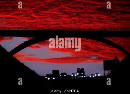 Commuters travel at sunset beneath a highway bridge silhouetted against a brilliant red sky. Picture by Jim Holden. Stock Photo