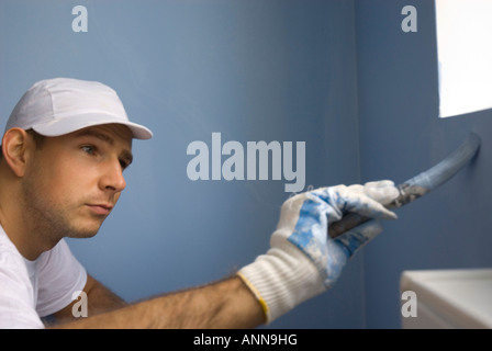 male painter worker concentrates on painting blue interior wall Stock Photo