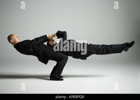 Profile of two male acrobats in business suits performing Stock Photo