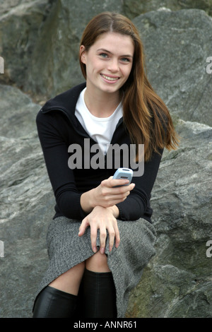 Attractive female sitting on rocks smiling holding a mobile phone Stock Photo