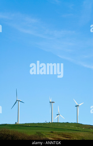 Vertical view of common three bladed wind turbines perched on a hill at a wind farm against a bright blue sky Stock Photo