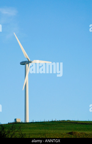 Vertical view of common three bladed wind turbine perched on a hill at a wind farm against a bright blue sky Stock Photo