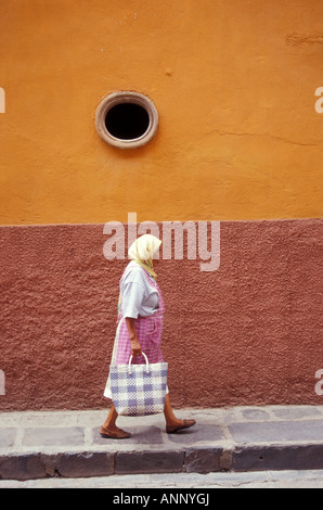 Woman walking along the sidewalk carrying a shopping bag in San Miguel de Allende, Guanajuato, Mexico Stock Photo