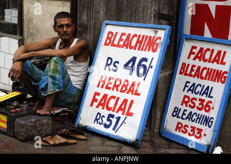 A man offers shoe shines and facial bleaching on a street in central Kolkata. Facial bleaching helps achieve a pale complexion. Stock Photo