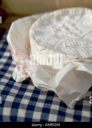 Camembert cheese round in waxy paper on a blue gingham tablecloth. Stock Photo