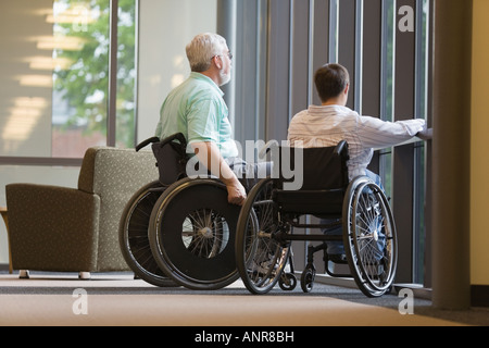 Middle-aged man and a middle aged woman sitting in wheelchairs in a library Stock Photo