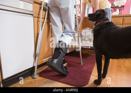 Low section view of a woman on crutch standing in the kitchen near a dog Stock Photo