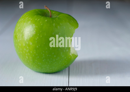 Granny Smith apple with bite taken out on blue wooden table Stock Photo