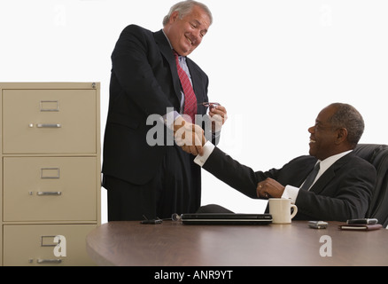 Two businessmen shaking hands and smiling in an office Stock Photo