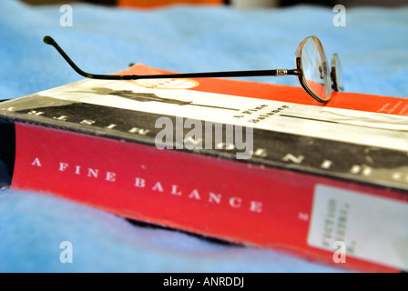 A pair of glasses sits upon a novel which lays upon a bed blanket Stock Photo