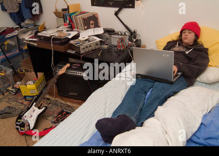A teenage boy using a laptop computer in his very untidy bedroom Stock Photo
