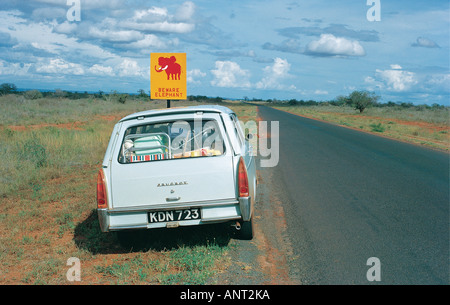 Peugeot 404 station wagon parked on the main Nairobi Mombasa road next to a road sign reading BEWARE ELEPHANT Kenya East Africa Stock Photo