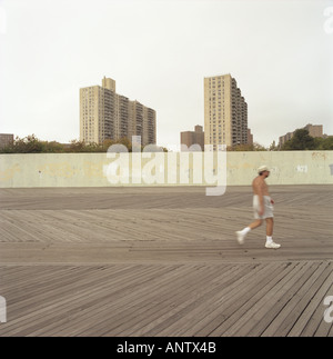 One mature person is jogging along the pathway in front of the sea side Coney Island New York series of buildings Stock Photo