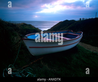 a small rowing boat in the foreground with a path leading down to the seashore coast at sunset dusk sundown on the isle of wight Stock Photo