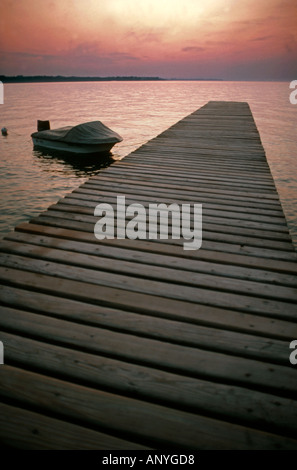 Small speedboat tethered to a wooden jetty with dramatic sunset on the water Stock Photo