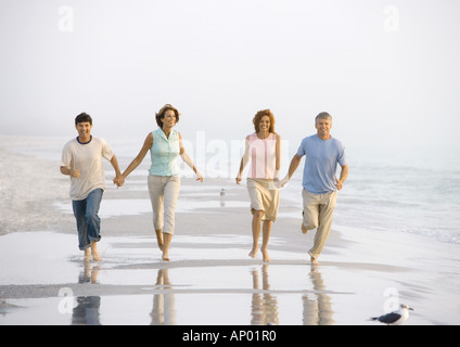 Two mature couples walking on beach, holding hands Stock Photo