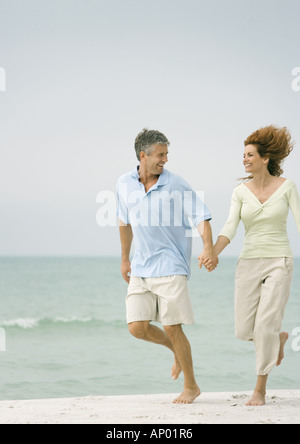 Mature couple running on beach, hand in hand Stock Photo
