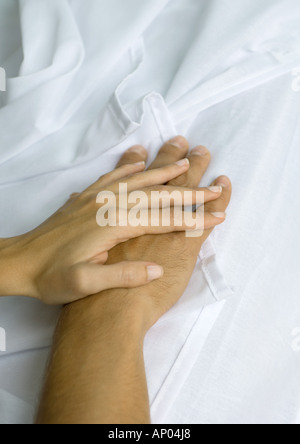 Woman's hand on top of man's, on sheets Stock Photo