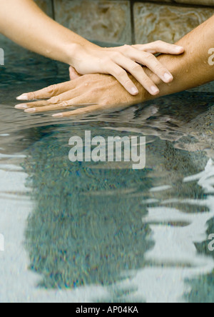 Woman's and man's hands on surface of pool water together Stock Photo
