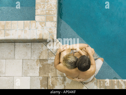 Couple sitting on edge of pool together Stock Photo
