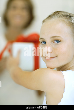 Girl holding out present to woman, smiling over shoulder at camera Stock Photo