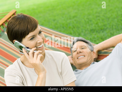 Woman using cell phone while man lounges on hammock Stock Photo