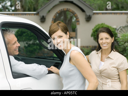 Two women standing next to vehicle with man inside, smiling Stock Photo