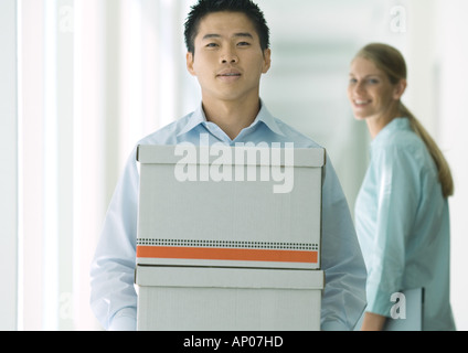 Man carrying boxes in hallway, female colleague watching Stock Photo