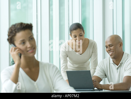 Office scene, two coworkers using laptop while woman in foreground uses cell phone Stock Photo
