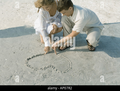 Couple drawing heart in sand Stock Photo