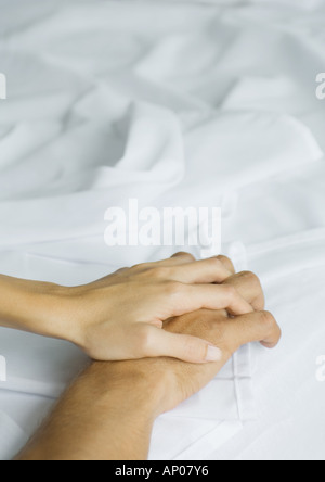 Couple holding hands on sheets, close-up Stock Photo