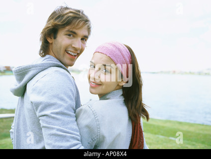 Young couple standing by lake, smiling over shoulder at camera Stock Photo
