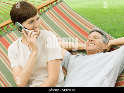 Mature couple lounging in hammock, woman using cell phone Stock Photo