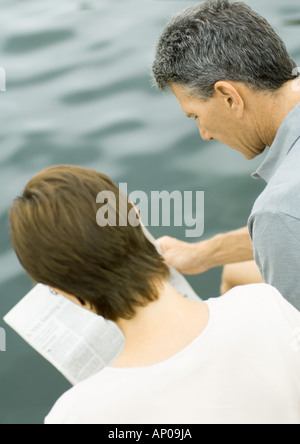 Couple reading newspaper together, water in background Stock Photo