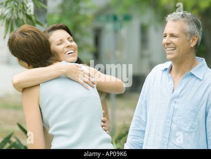 Two woman hugging while man watches Stock Photo