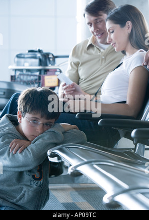 Family sitting in airport lounge, boy on floor, leaning on seat Stock Photo