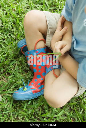 Child sitting, holding blades of grass Stock Photo