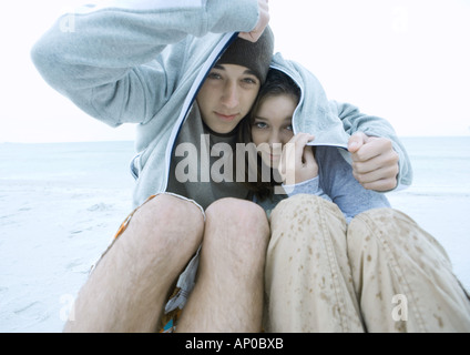 Couple covering heads with jacket in the rain, on beach Stock Photo
