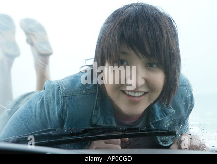 Woman lying on hood of car, looking through windshield Stock Photo
