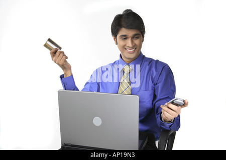 ANG200144 Executive  holding laptop on his lap in one hand credit card and other mobile phone Stock Photo