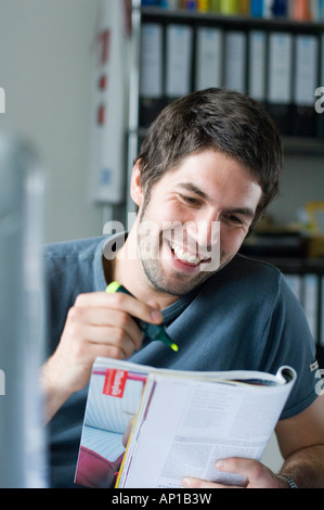 Smiling young man reading magazine, holding highlighter Stock Photo