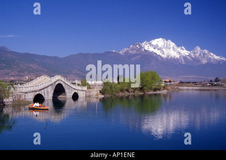 Man in small boat sails by picturesque bridge over small lake near Lijiang,Yunnan province,China. Stock Photo