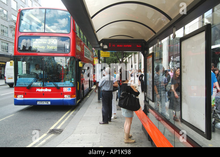 London Oxford Street shoppers number 390 bus at stop with shelter seats and electronic indicator board Stock Photo