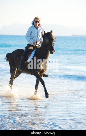 woman riding a black horse on the beach Stock Photo