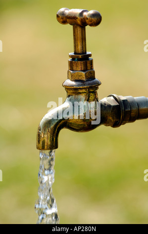 an old fashioned style of brass water tap outside oudoors running wasting water turned and left on running Stock Photo